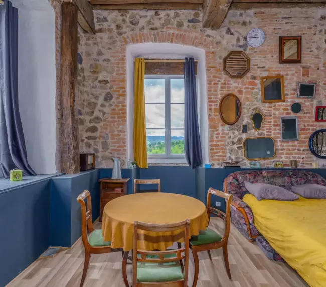 Chambre avec coin salon au Château de Gorze – mur en brique, collection de miroirs et vue sur la campagne