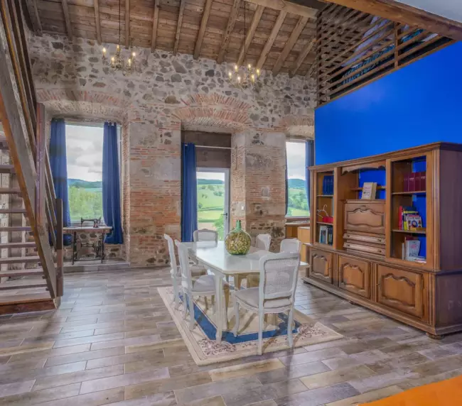 Séjour lumineux double hauteur du gîte du Château de Gorze – vue sur la campagne, escalier en bois et mur en brique
