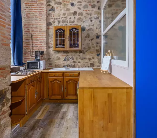 Cuisine équipée en bois massif du gîte du Château de Gorze avec mur en brique et pierre apparente