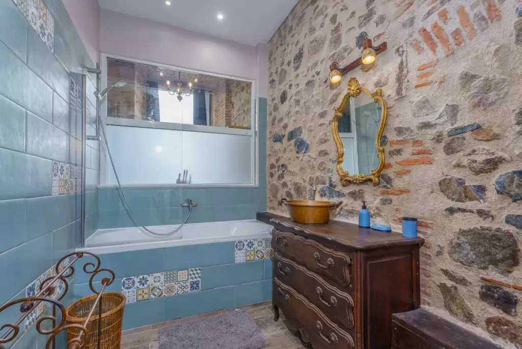 Salle de bain rustique chic du Château de Gorze – baignoire, carrelage bleu et mur en pierre apparente
