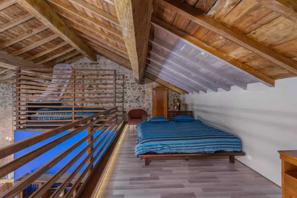 Chambre mezzanine en duplex au Château de Gorze – lit double sous charpente apparente et mur en pierre