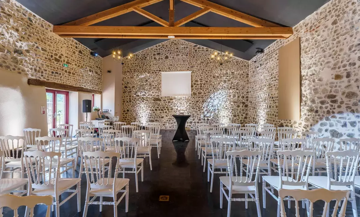 Salle de réception du Château de Gorze en configuration conférence – éclairage d'ambiance, mur en pierre apparente et charpente en bois