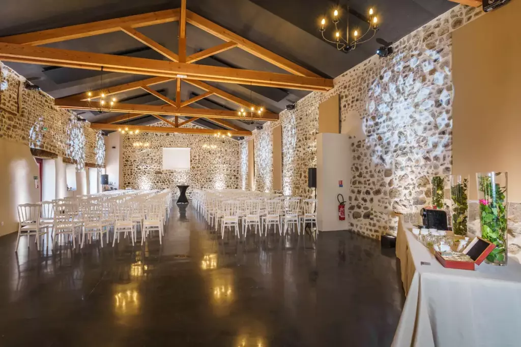Salle de réception du Château de Gorze en configuration conférence – chaises blanches en rangées, écran de projection et mur en pierre