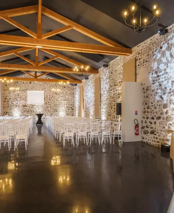 Salle de réception du Château de Gorze en configuration conférence – chaises blanches en rangées, écran de projection et mur en pierre