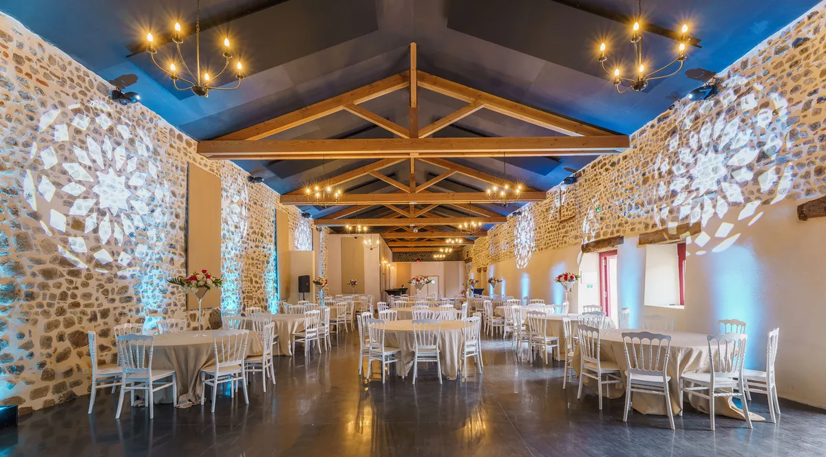 Salle de réception du Château de Gorze en configuration banquet – éclairage bleu, mur en pierre apparente et charpente en bois