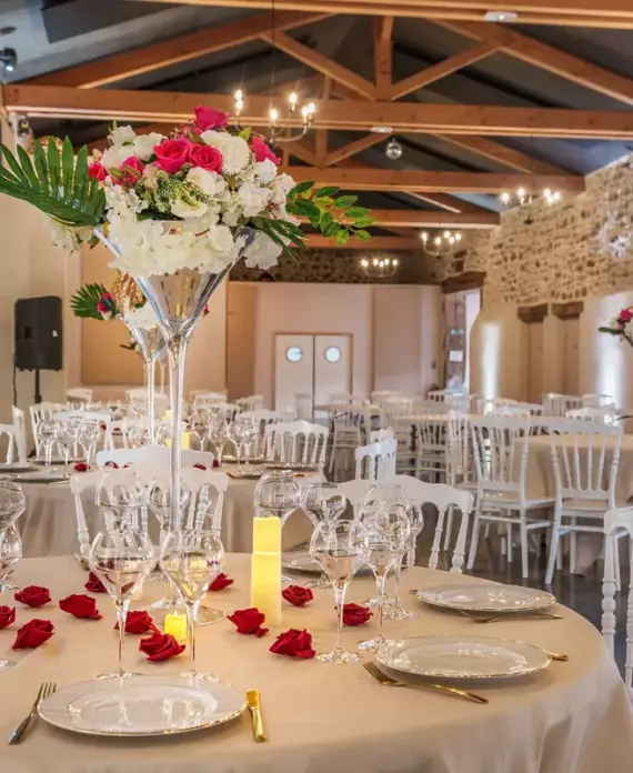 Salle de réception du Château de Gorze décorée pour un mariage – tables rondes, compositions florales et charpente en bois