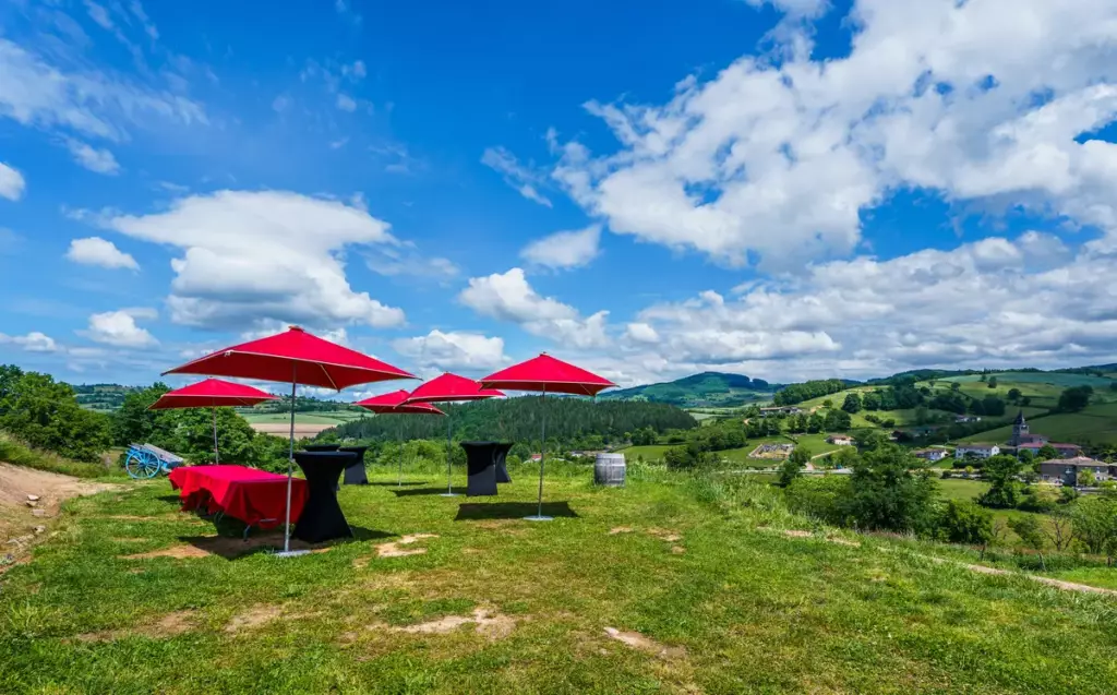 Espace cocktail extérieur du Château de Gorze – parasols rouges, tables hautes et vue panoramique sur la vallée