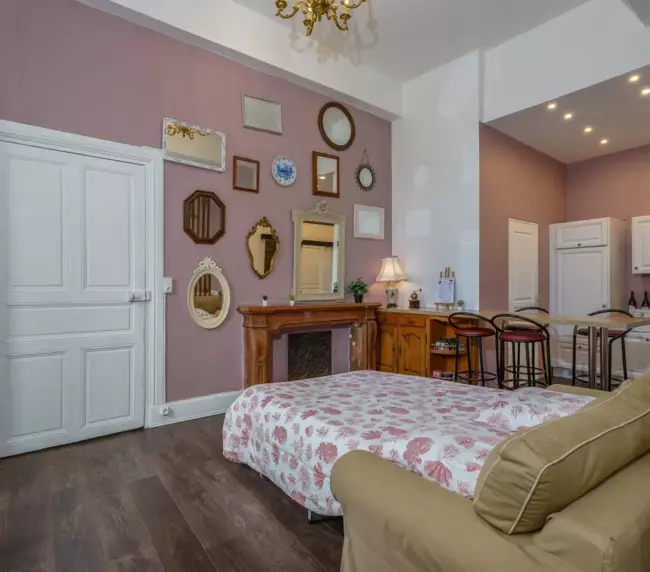 Studio du Château de Gorze avec lit double, cheminée ancienne, collection de miroirs et mur mauve