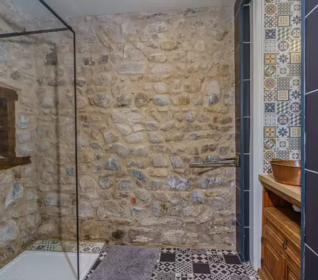 Salle de bain du gîte du Château de Gorze – douche à l'italienne, mur en pierre apparente et carrelage à motifs