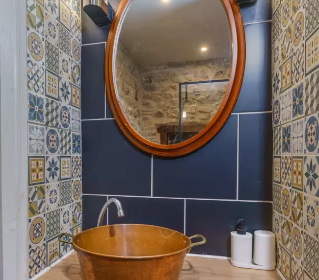 Vasque en cuivre sur plan de travail en bois dans la salle de bain du Château de Gorze – carrelage bleu et miroir ovale