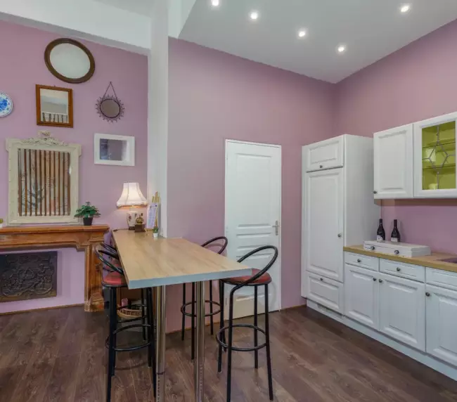 Cuisine équipée du gîte du Château de Gorze – bar avec tabourets, façades blanches et mur mauve
