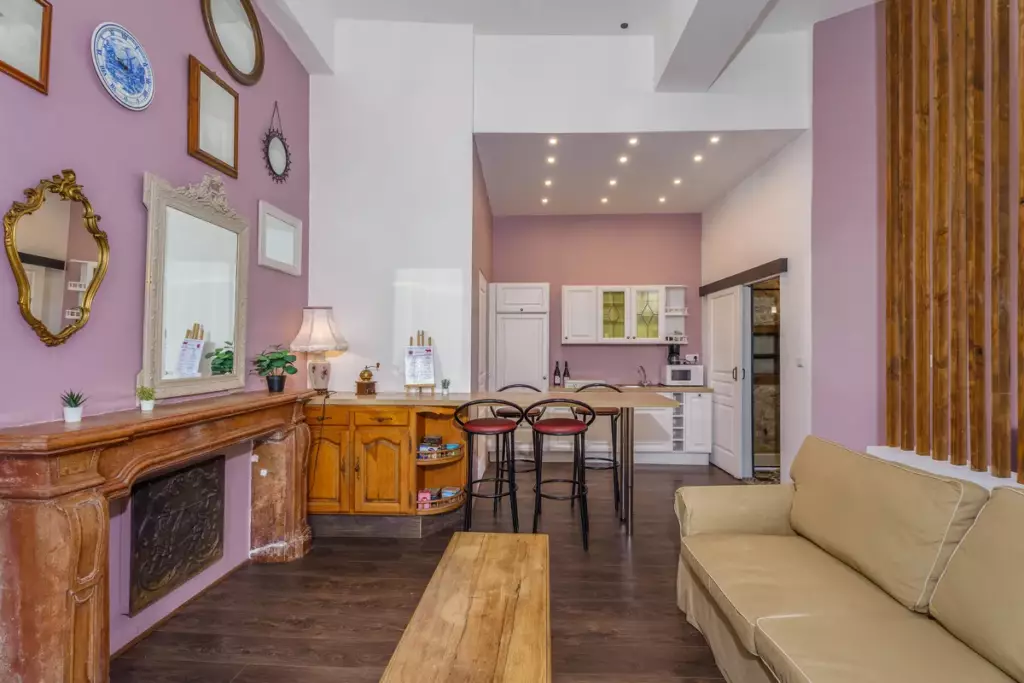 Séjour et cuisine ouverts du gîte du Château de Gorze – cheminée ancienne, mur mauve et espace bar