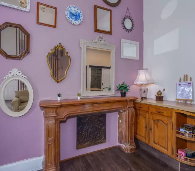 Salon du gîte du Château de Gorze avec cheminée en bois sculpté, mur mauve et collection de miroirs anciens