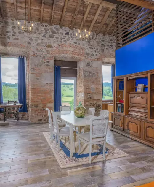 Séjour lumineux double hauteur du gîte du Château de Gorze – vue sur la campagne, escalier en bois et mur en brique