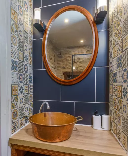 Vasque en cuivre sur plan de travail en bois dans la salle de bain du Château de Gorze – carrelage bleu et miroir ovale