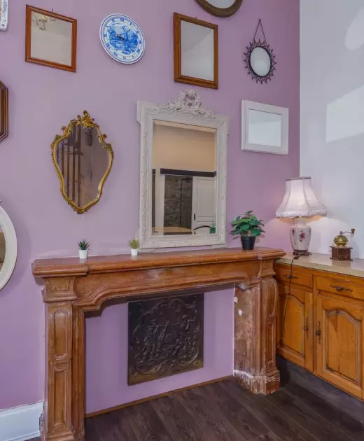 Salon du gîte du Château de Gorze avec cheminée en bois sculpté, mur mauve et collection de miroirs anciens